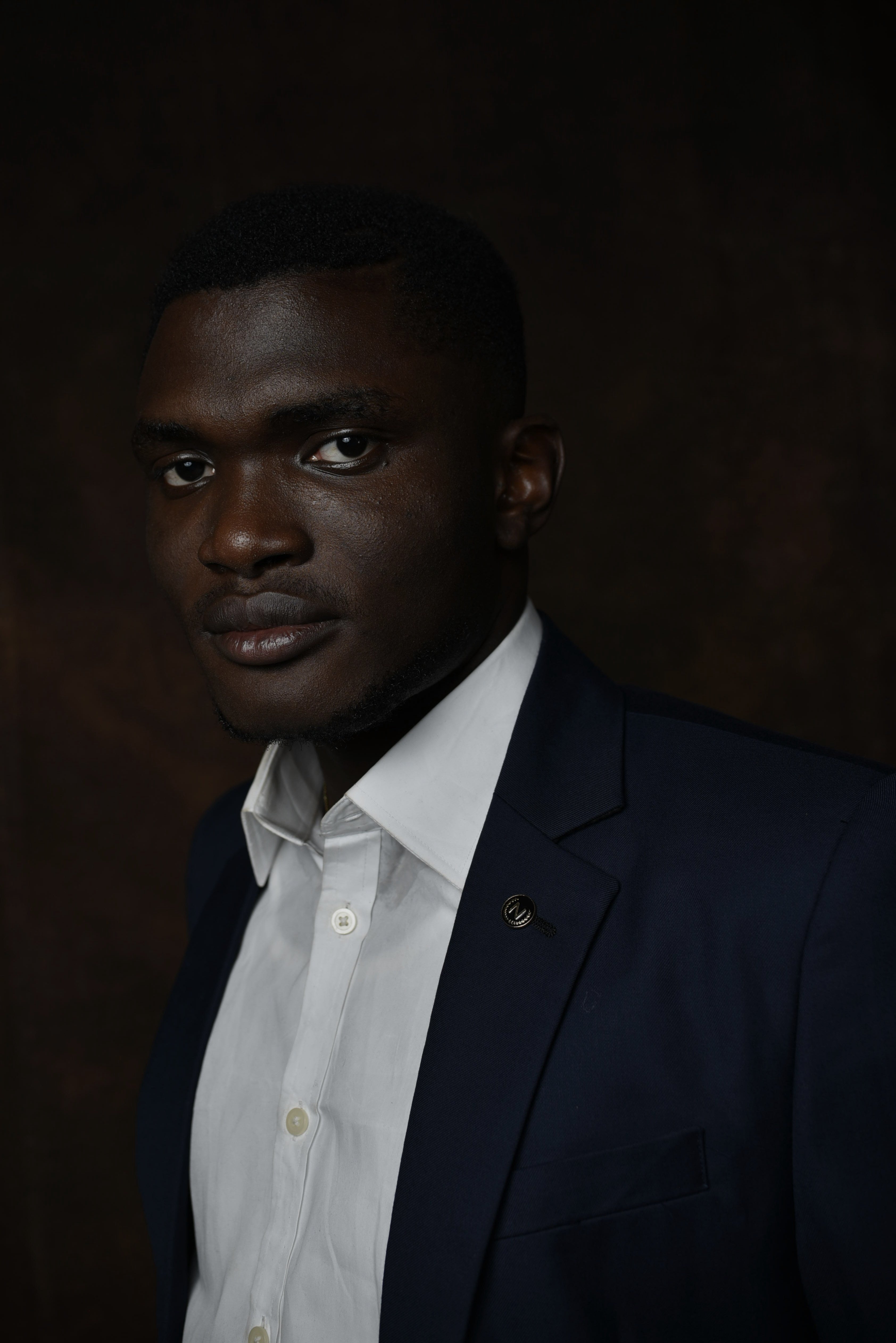 Testimony Adekoya — navy suit, warm studio portrait